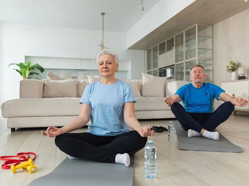 An elderly couple engaged in a yoga session in their living room