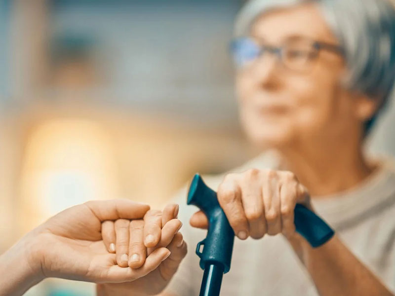 An elderly woman gently holds the hand of a young woman,