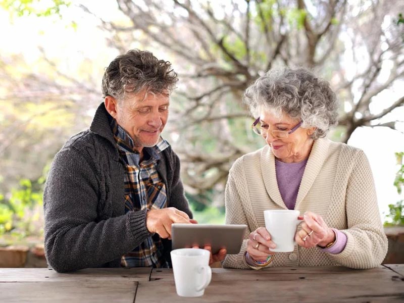 A senior couple at a table, focused on a tablet, enjoying each other's company