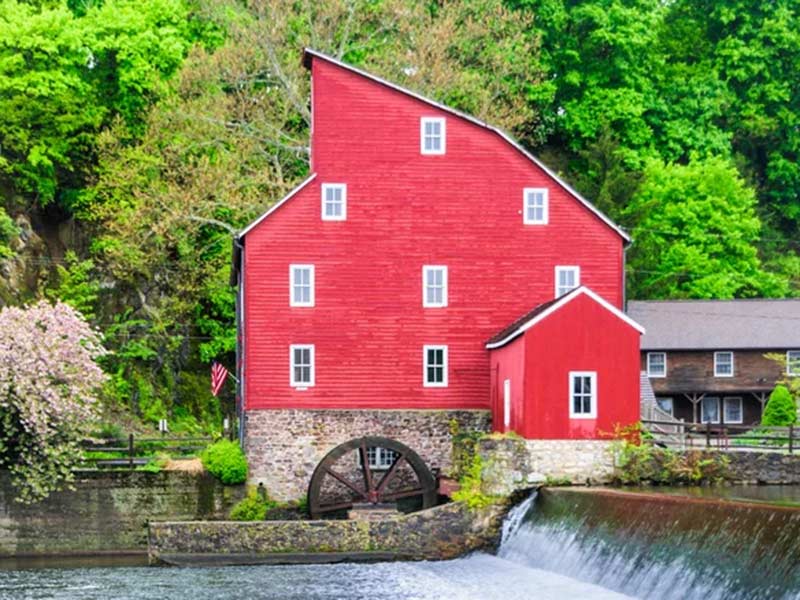 A red mill stands beside a river, with a waterfall cascading nearby